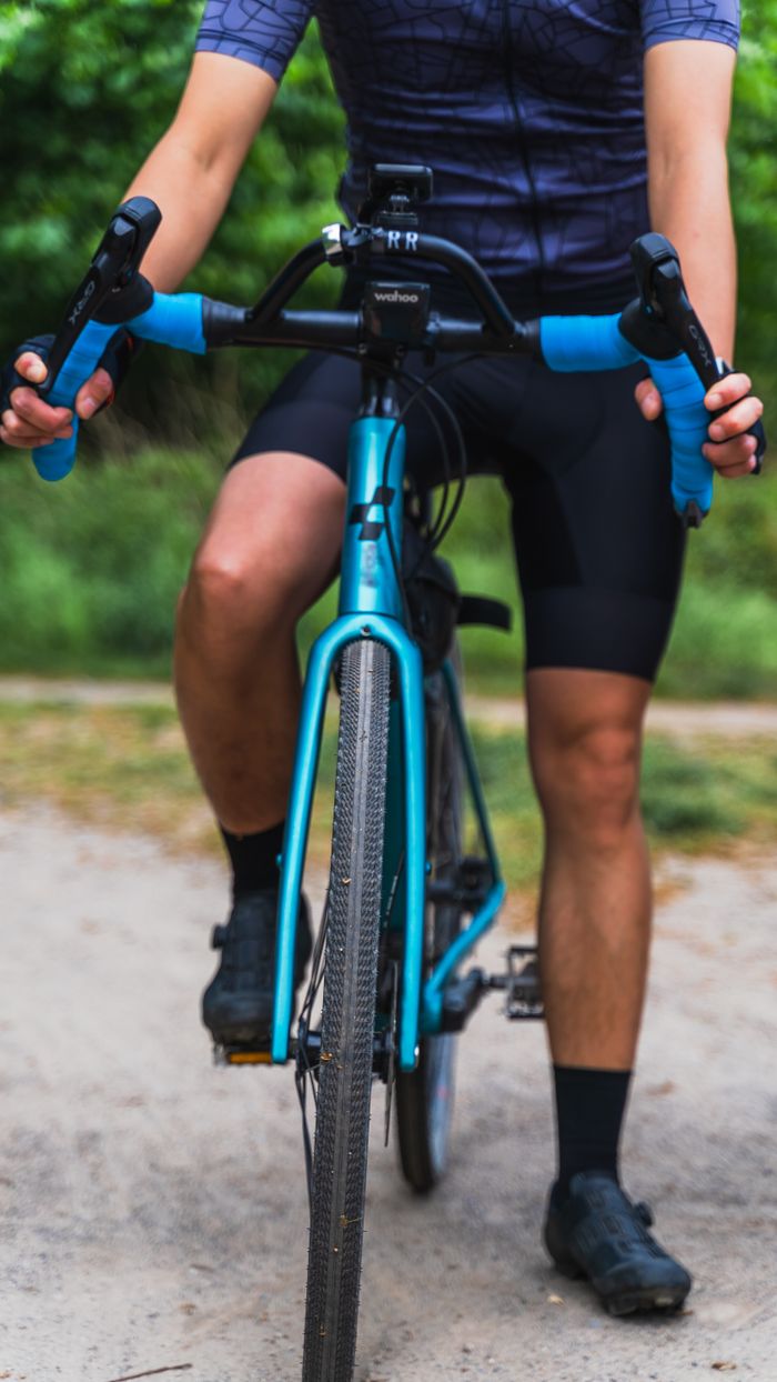 Close-up of a cyclist riding a blue bicycle on a gravel path in a park setting.